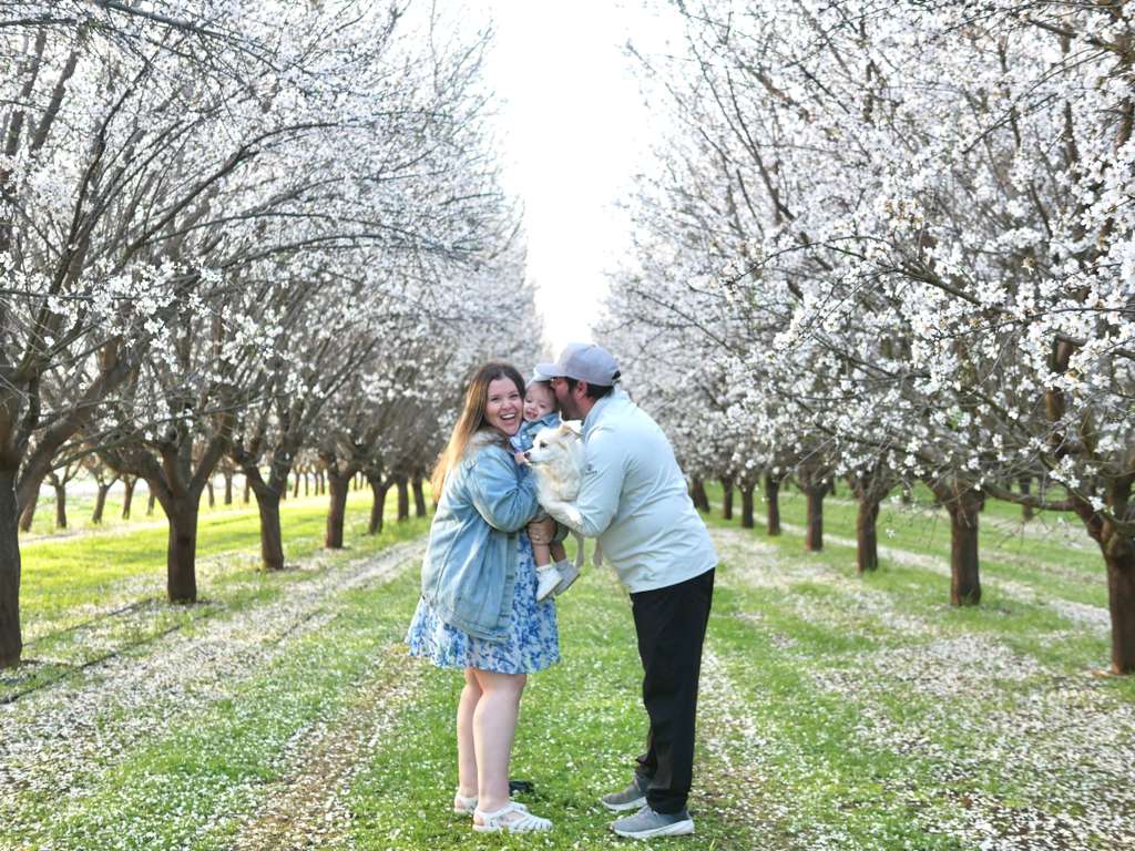 Two people standing in a blossoming orchard with a dog.